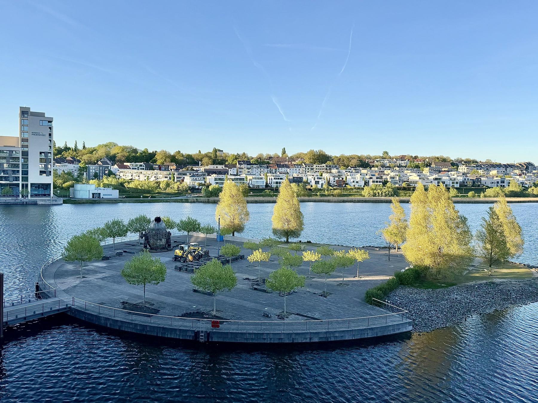 Phoenixsee Dortmund — Blick auf die Kulturinsel mit jungen Bäumen, dahinter die Hörder Wohnbebauung am Hang